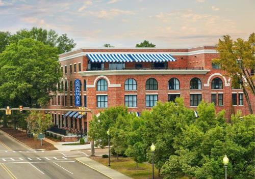 A brick hotel with blue and white awnings, surrounded by trees, on a street with traffic lights.