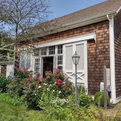 A charming wooden house with a flower garden, featuring a lantern and large windows with white shutters.