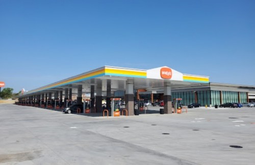 A modern gas station with multiple fueling stations and a convenience store under a clear blue sky.