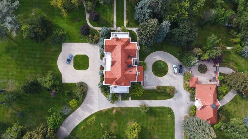 Aerial view of a large house with a red roof, surrounded by green lawns and winding driveways.