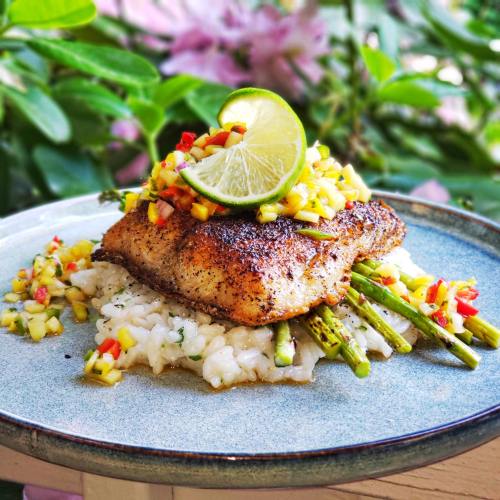 A beautifully plated fish dish topped with mango salsa and lime, served on a bed of risotto and asparagus.