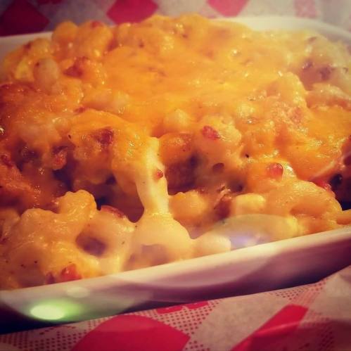 A close-up of creamy macaroni and cheese topped with melted cheese, served in a white dish on a red-checkered background.