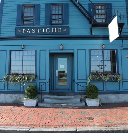 A blue building with the sign "PASTICHE," featuring flower boxes and a welcoming entrance.
