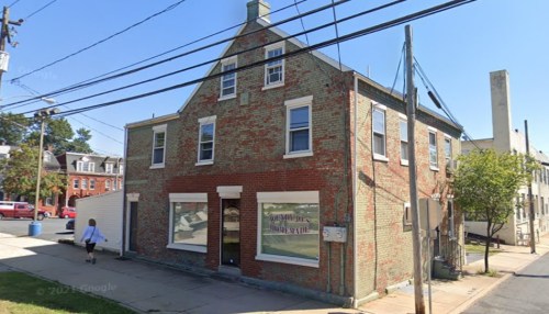 A brick building with multiple windows, located at a street corner, with a person walking by and power lines overhead.