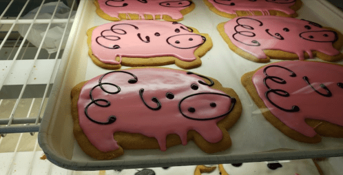 A tray of pink pig-shaped cookies with black icing details, displayed in a bakery.