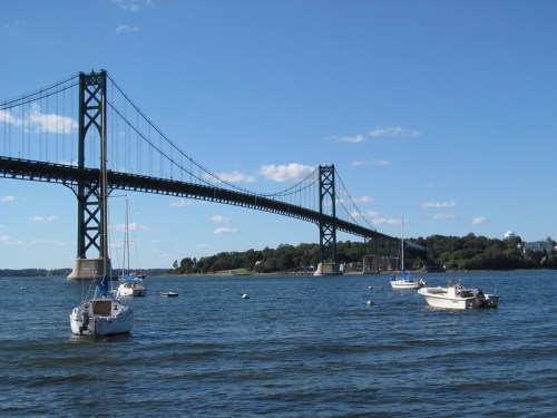 A scenic view of a bridge spanning a river, with several boats floating nearby under a clear blue sky.