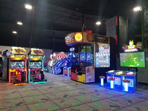 A vibrant arcade with various colorful games, including racing and skill-based machines, under dim lighting.