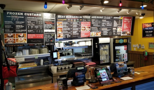 Menu board at a fast-casual restaurant featuring burgers, frozen custard, and various sides, with a vibrant decor.