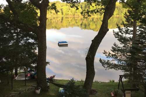 A serene lake scene framed by trees, with a small blue boat floating on the calm water reflecting the sky.