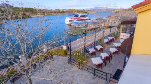 Scenic view of a lakeside restaurant with tables, a boat docked, and mountains in the background.