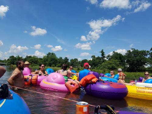A group of people relax on colorful inner tubes in a river under a blue sky with fluffy clouds.