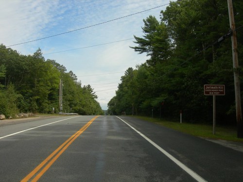 A quiet road lined with trees, featuring a sign for Jefferson Hill and a clear blue sky above.
