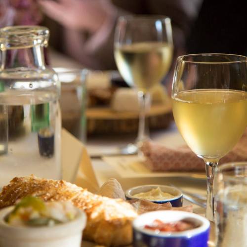 A table setting with a glass of white wine, a water carafe, and a plate of food, creating a cozy dining atmosphere.