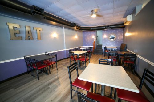 A cozy restaurant interior with tables and chairs, featuring an "EAT" sign on the wall and a modern decor.