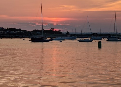A serene sunset over a calm harbor, with sailboats gently bobbing on the water.
