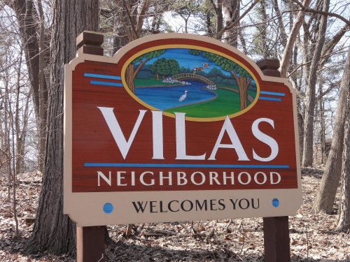 Sign for Vilas Neighborhood, featuring a scenic design with a bridge and water, surrounded by trees.