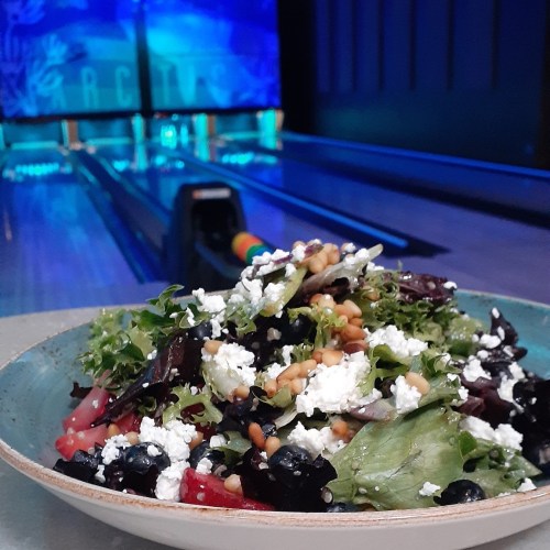 A colorful salad with greens, cheese, and nuts, set against a bowling alley backdrop.