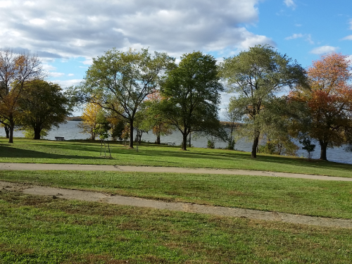 A serene park scene with trees and a river in the background under a partly cloudy sky.