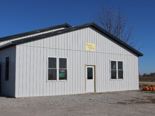 A white metal building with a sign, windows, and a door, set against a clear blue sky.