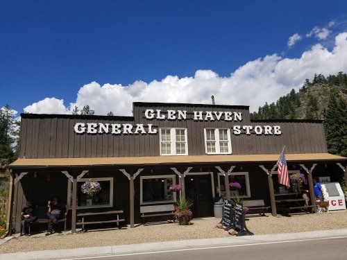 A rustic general store with "Glen Haven General Store" sign, surrounded by trees and blue sky, with people sitting outside.