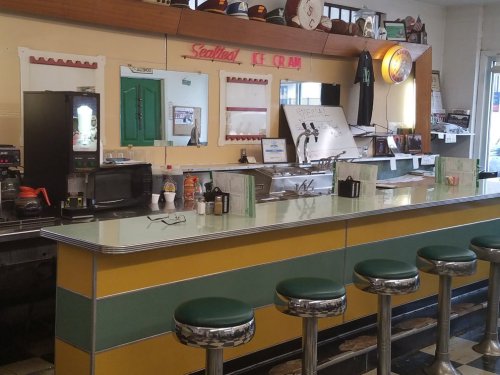 A retro diner counter with green stools, a coffee machine, and vintage decor, evoking a nostalgic atmosphere.