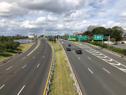 A view of a highway with two lanes, green road signs, and cars traveling under a partly cloudy sky.
