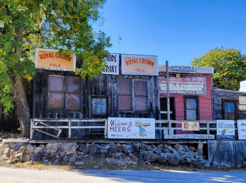 Old wooden building with signs for "Royal Crown" and "Meers," featuring a rustic, weathered facade and a welcoming entrance.