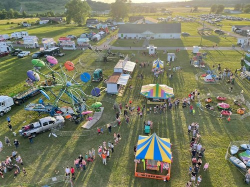 Aerial view of a lively fair with rides, food trucks, and crowds enjoying the festivities on a sunny day.