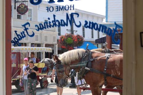 A view through a window showing a horse-drawn carriage and people walking in a vibrant, historic town.