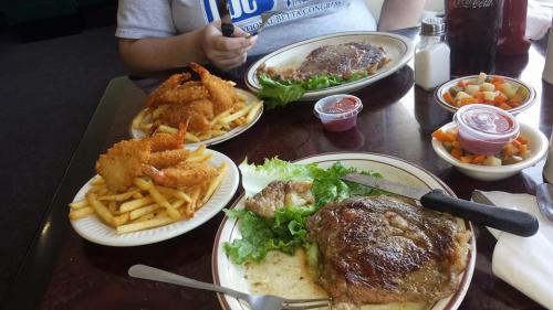 A table with two plates: one with a steak and salad, the other with shrimp and fries, plus a side of mixed vegetables.