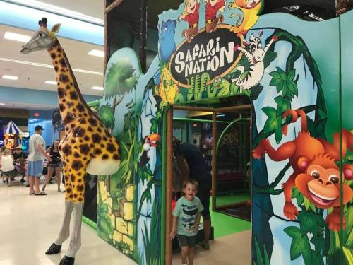 A child exits a colorful play area themed like a safari, featuring a giraffe and jungle animals on the walls.