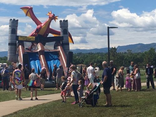 A crowd gathers around a large dragon-themed inflatable slide at an outdoor event, with mountains in the background.