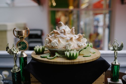 A decorative dessert topped with meringue, surrounded by lime slices and trophies on a wooden display.