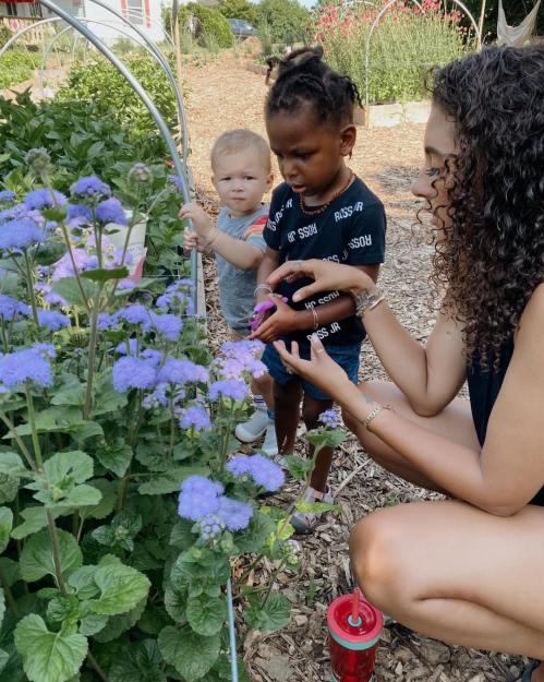 A woman and two children are tending to flowers in a garden, surrounded by vibrant purple blooms.