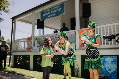 A lively scene at the Key West Lighthouse with performers in green costumes engaging with a smiling child.