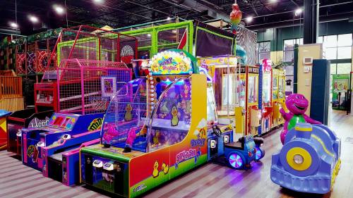 Colorful arcade games and attractions in a vibrant indoor play area, featuring bright lights and playful designs.