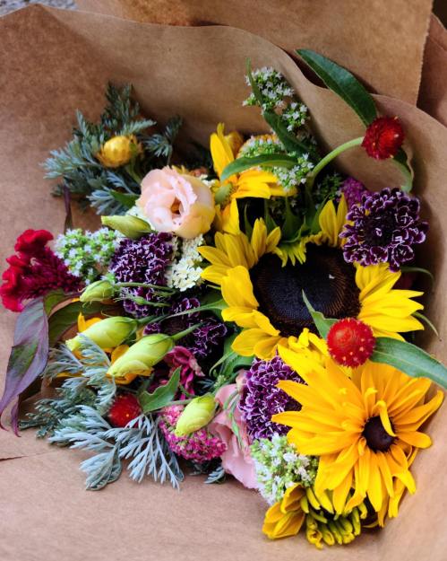 A vibrant bouquet of sunflowers, roses, and various colorful flowers wrapped in brown paper.