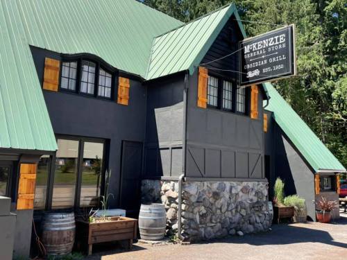 Exterior of McKenzie General Store with a green roof, stone base, and wooden accents, featuring a sign for Obsidian Grill.