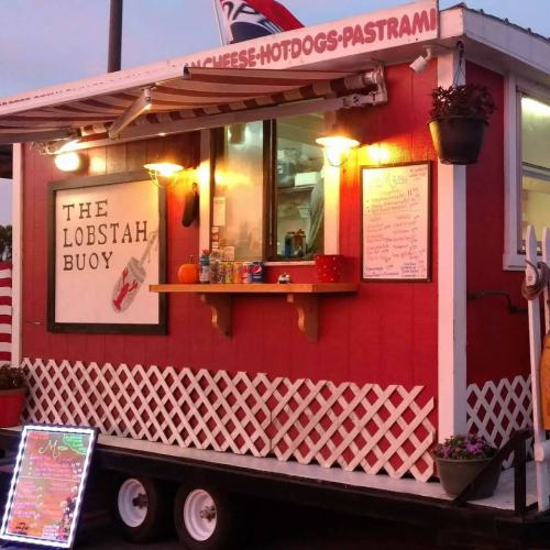 A food truck named "The Lobstah Buoy" with a red exterior, serving seafood and snacks, surrounded by decorative plants.