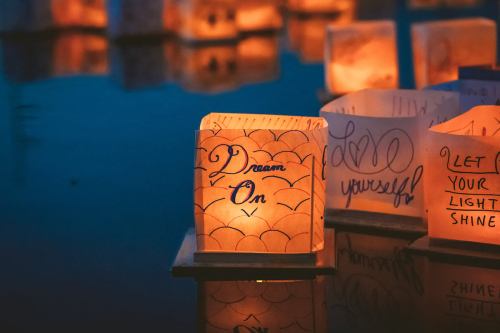 Glowing lanterns on water, featuring messages like "Dream On" and "Let Your Light Shine."