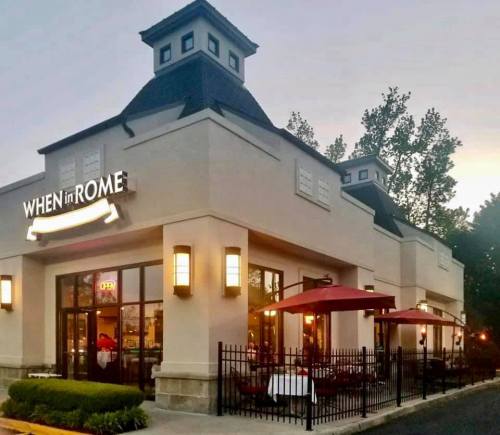 Exterior of a restaurant named "When in Rome," featuring outdoor seating and a welcoming atmosphere at dusk.