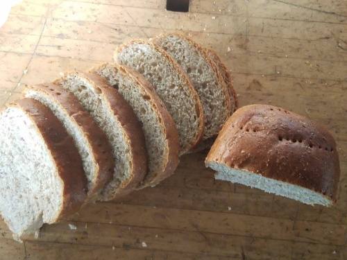 Sliced whole grain bread on a wooden surface, with one slice partially removed from the loaf.