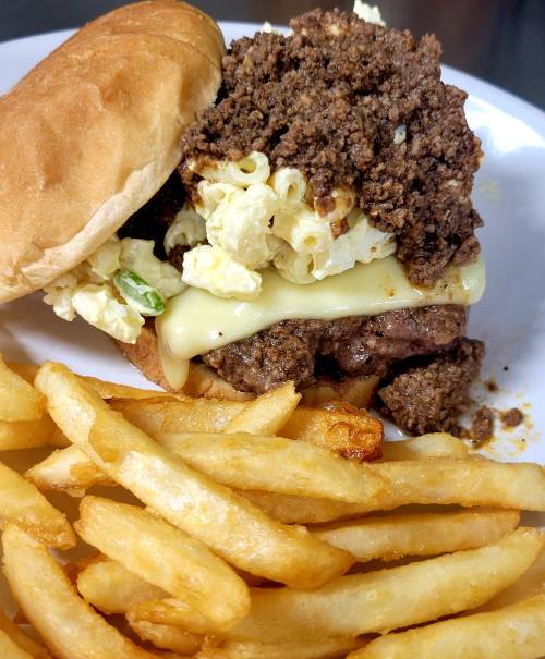 A burger topped with popcorn and ground meat, served with a side of golden French fries on a white plate.