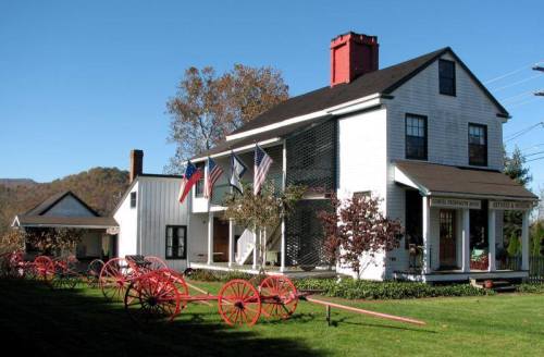Historic white house with a red chimney, surrounded by flags and vintage wagons on a grassy lawn.