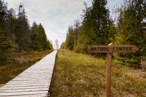 A wooden path leads through trees to a white building labeled "Nature Center," with a sign pointing the way.