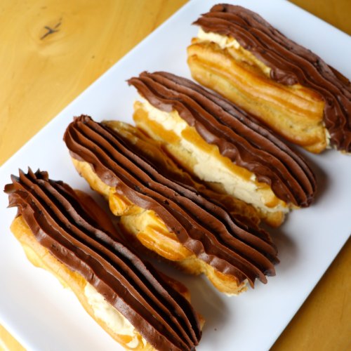 A plate of cream-filled eclairs topped with rich chocolate frosting.