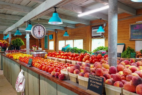 A vibrant market stall filled with colorful apples and peaches, featuring baskets and a scale under bright blue lights.