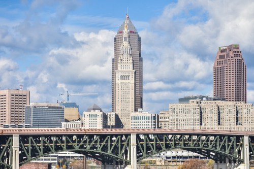 Cleveland skyline featuring tall buildings and a bridge under a partly cloudy sky.