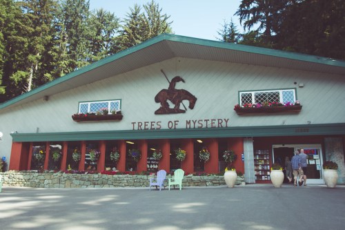 Exterior of the "Trees of Mystery" building, featuring flower boxes, a carved figure, and colorful chairs in front.