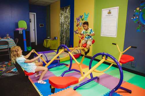 Two children play on colorful exercise equipment in a vibrant, playful room with butterfly decorations.